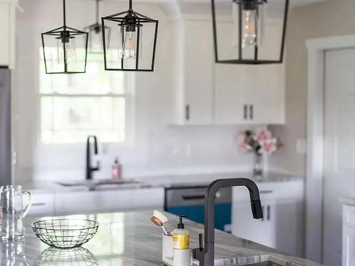 Kitchen with marble countertop, black fixtures, white cabinets, and geometric pendant lights.
