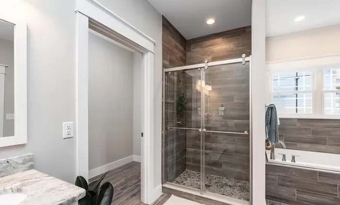 Modern bathroom with walk-in shower, dark wood-look tile, glass door, and white trim.