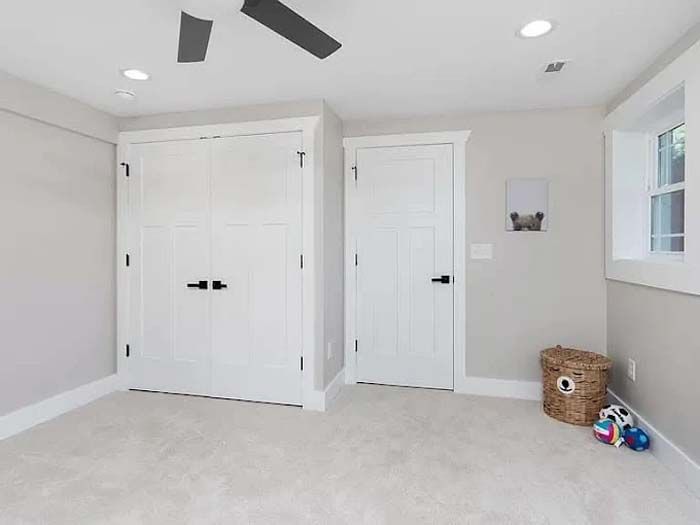 White-walled room with two doors and a small window. A basket, toys, and ceiling fan are present.
