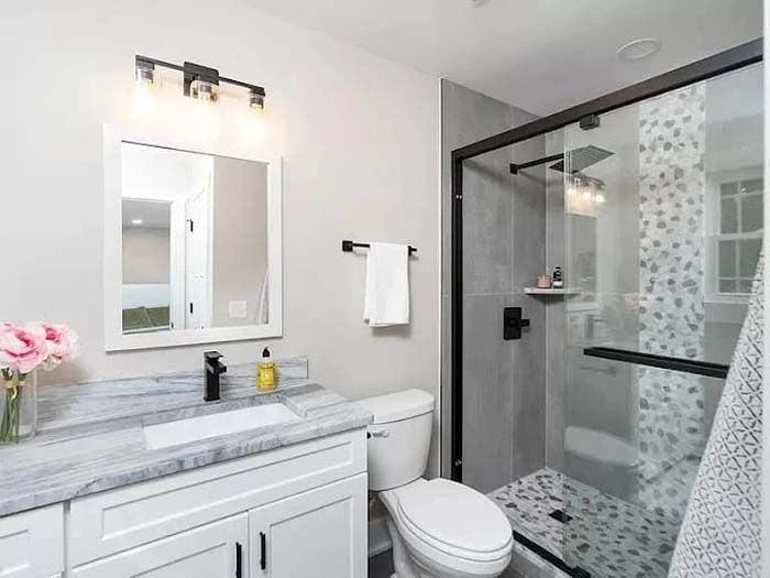 Modern bathroom with gray walls, white vanity, black fixtures, and a glass shower.