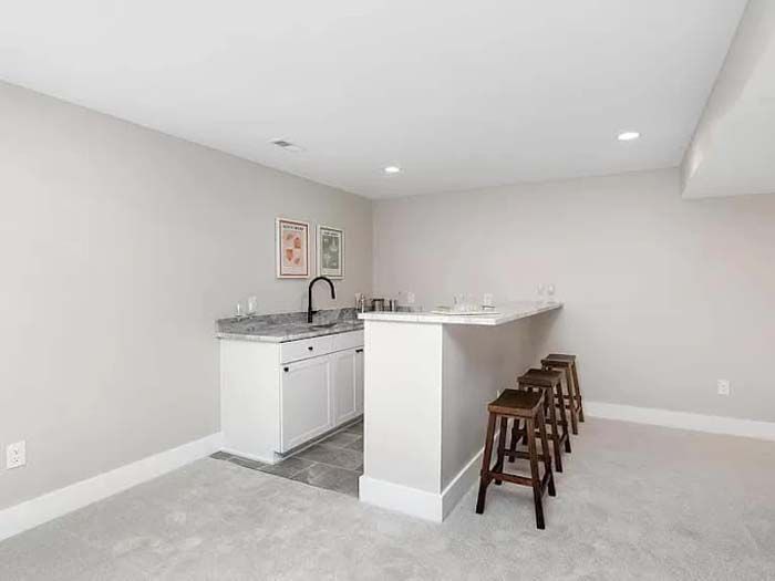 A small home bar with white cabinets, a granite countertop, and three wooden bar stools.