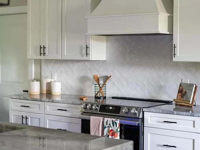 White kitchen with range, cabinets, and herringbone backsplash.