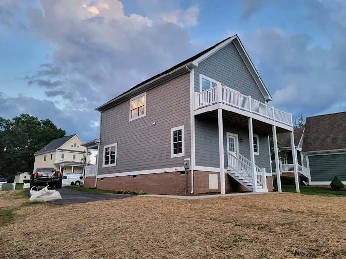 Two-story house with gray siding, white trim, and a second-floor balcony. Brick base. Cloudy sky.