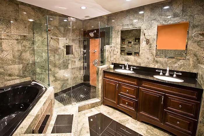 Luxurious bathroom with dark wood cabinets, stone walls, glass shower, and black bathtub.
