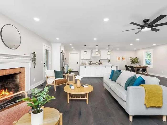 Open-concept living space with a fireplace, kitchen, and dining area. Neutral colors, modern furniture, and a ceiling fan.