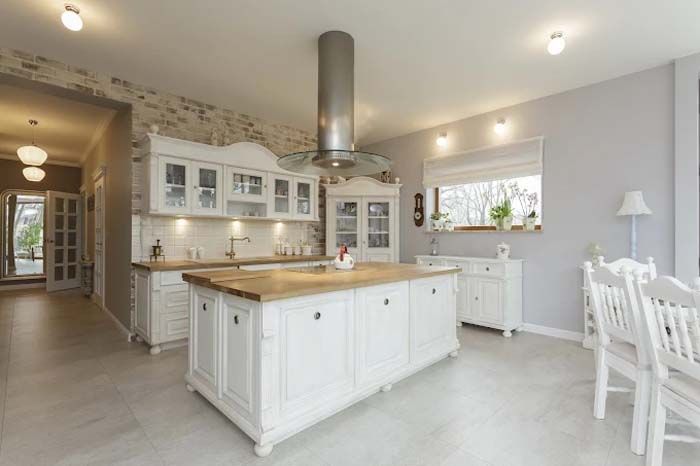 White kitchen with island and cabinetry; stone wall, wooden countertop, light gray walls, and bright lighting.