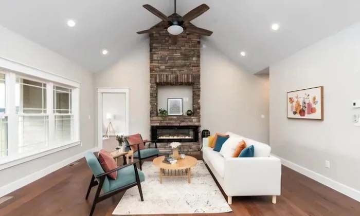 Living room with stone fireplace, white sofa, blue chairs, and wood flooring.