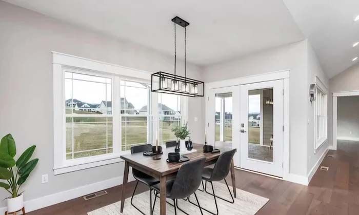 Dining room with table, chairs, windows, and chandelier; neutral tones and outdoor view.