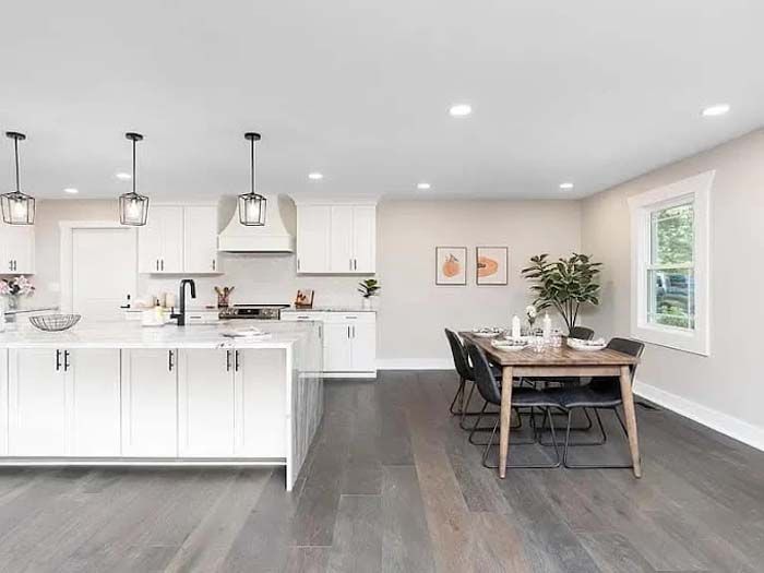 Modern kitchen with white cabinets, island, and dining area with wooden table and chairs.