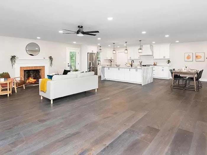 Open-concept living space with fireplace, kitchen island, dining area, and gray wood flooring.