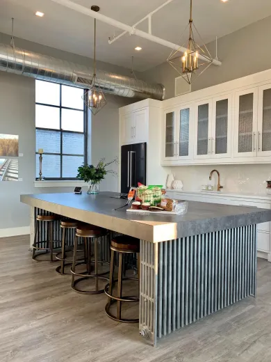 Modern kitchen with a large island, metal stools, and white cabinets in a bright industrial-style space