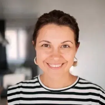 Smiling person in a black-and-white striped shirt, standing indoors with a softly blurred background