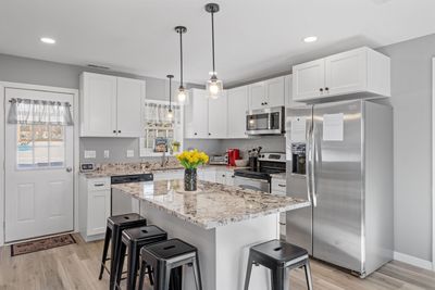 Modern white kitchen with granite island, stainless appliances, and black stools