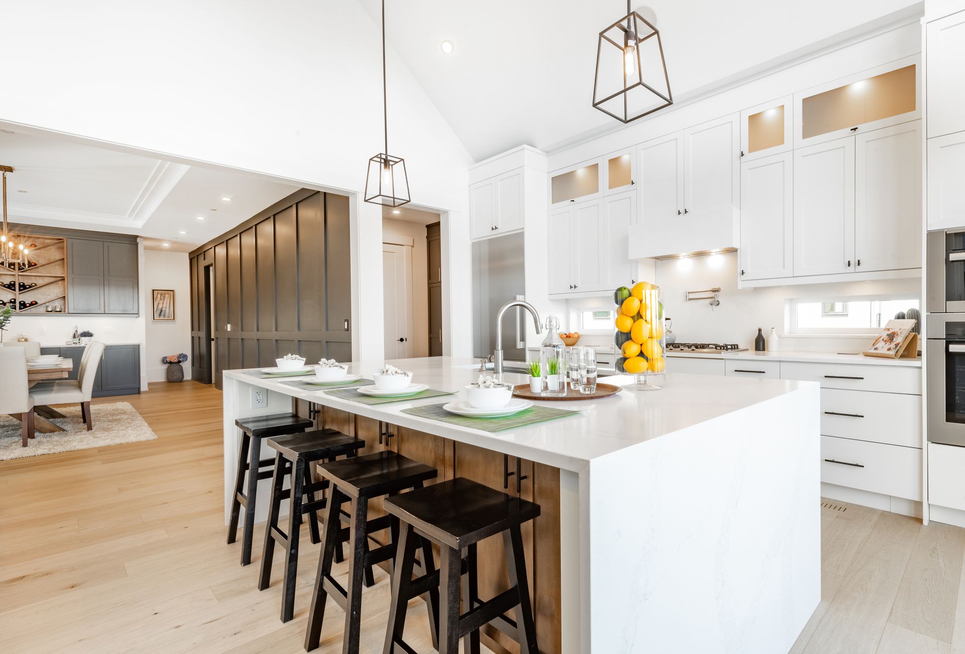 Bright modern kitchen with white cabinets, large island, and black stools in an open living space