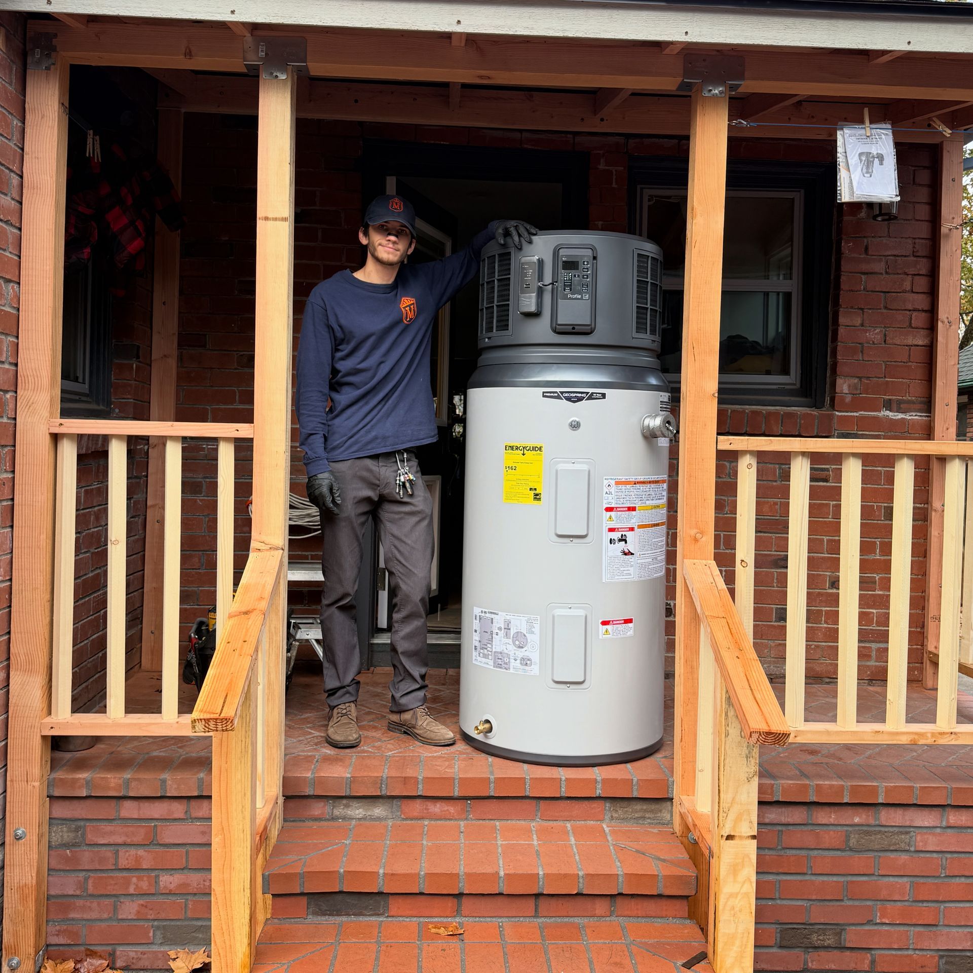 Person standing on a porch beside a large water heater or tank in a brick doorway.