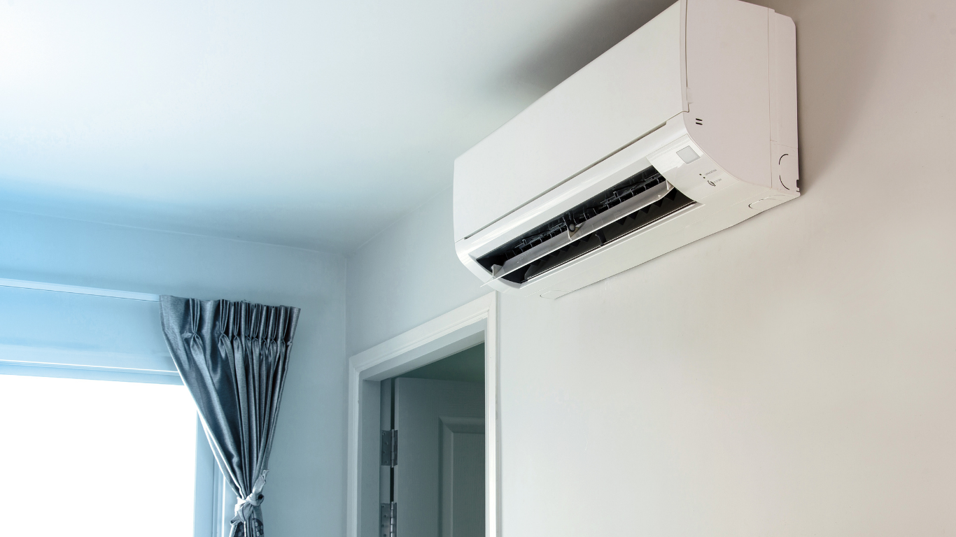 White wall-mounted air conditioner above a doorway in a bright room with a window and curtains