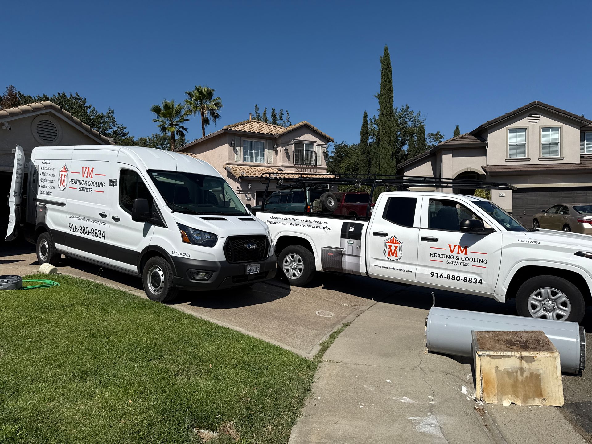 Two white work trucks parked in a suburban driveway beside a house