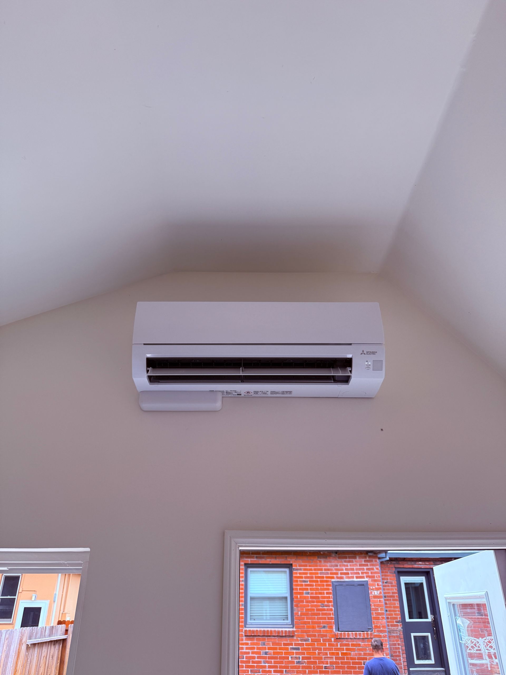 White wall-mounted air conditioner above two windows in a room with a high sloped ceiling