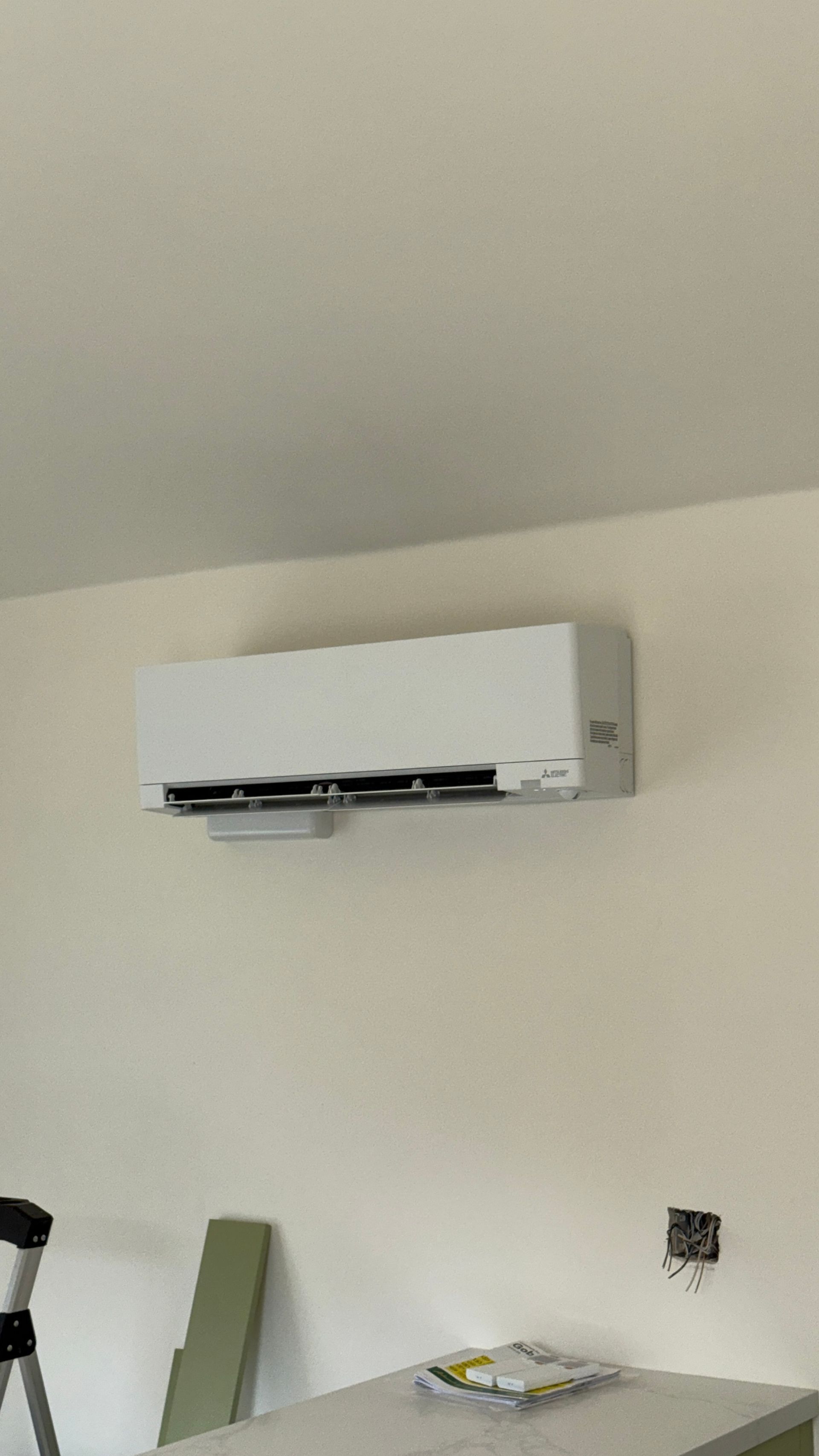 Wall-mounted air conditioner above a white wall with a small table below.