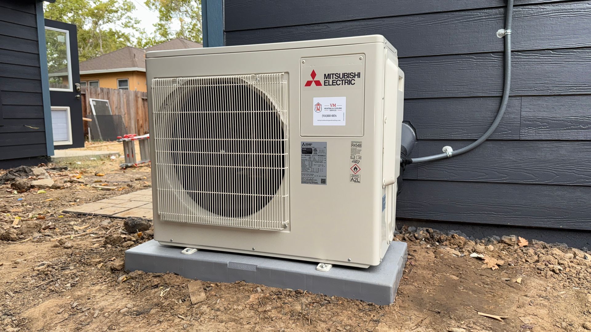 Outdoor Mitsubishi mini-split AC unit beside a dark house wall on a concrete pad