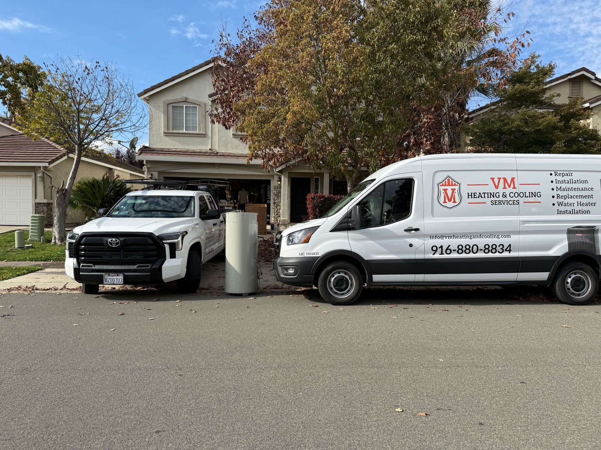 White pickup and service van parked in a suburban driveway outside a house on a sunny day