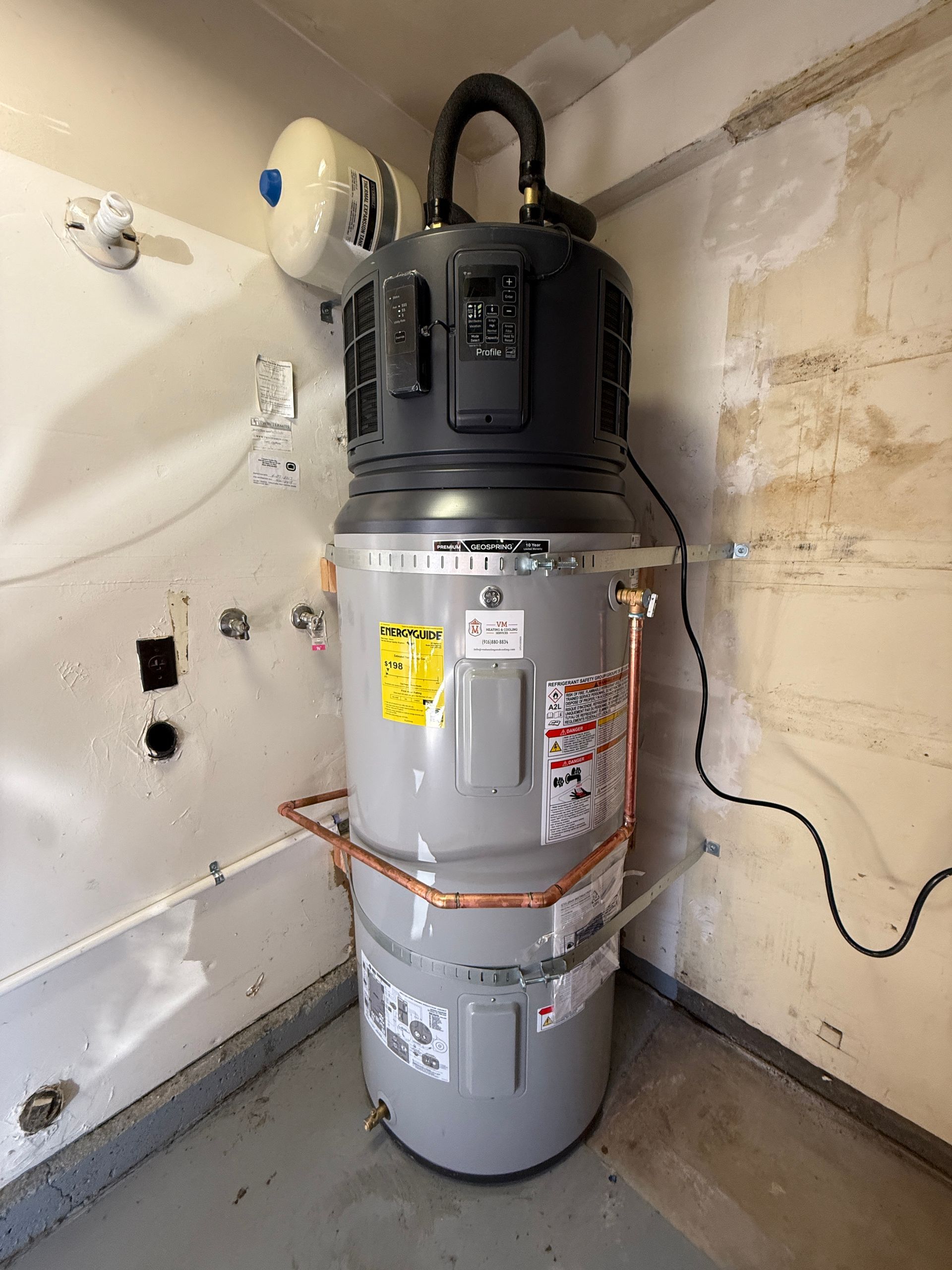 Water heater in a utility closet with exposed pipes and a wall-mounted expansion tank.