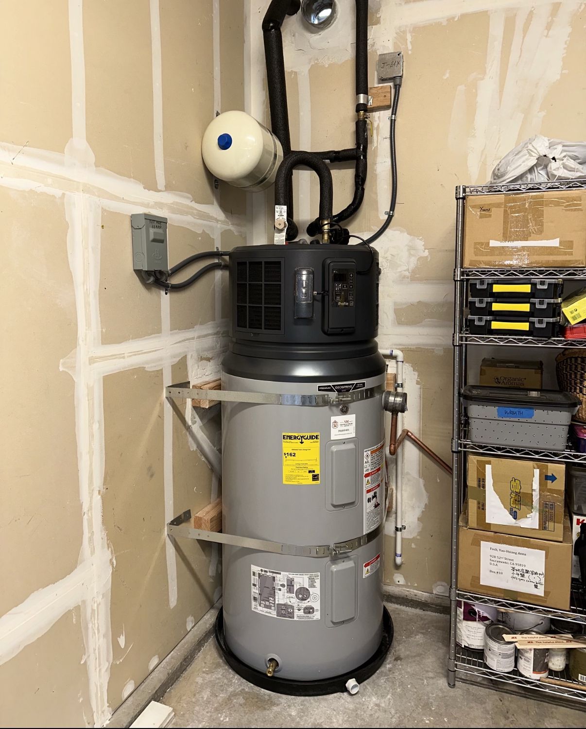 Water heater and furnace in a small utility closet with shelves and exposed pipes.