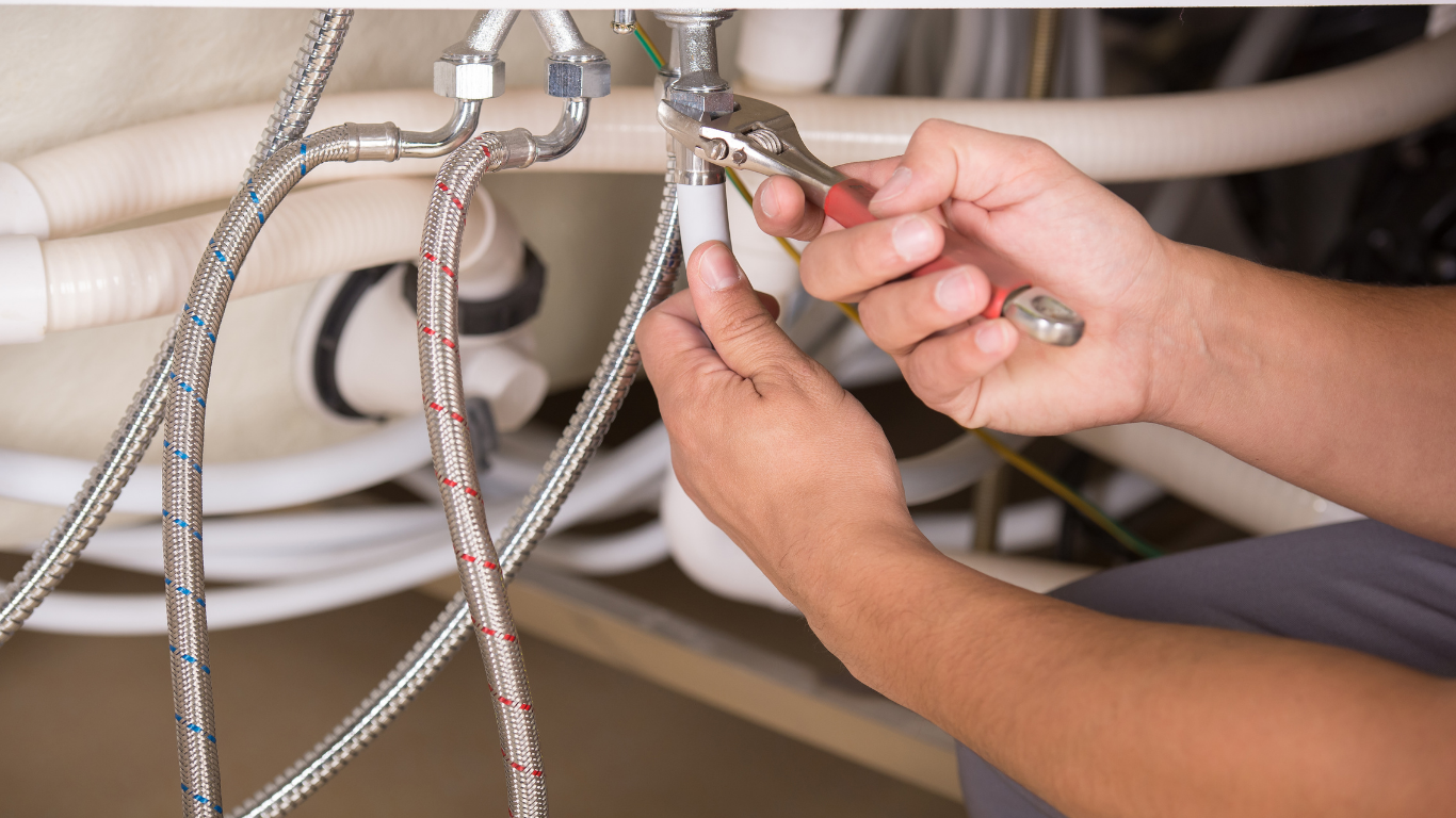 Hands tightening a silver braided faucet hose under a sink with a wrench