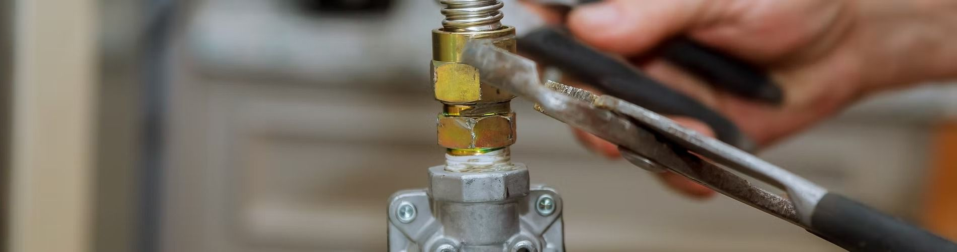 Hands tightening a brass valve on a metal gas line with pliers