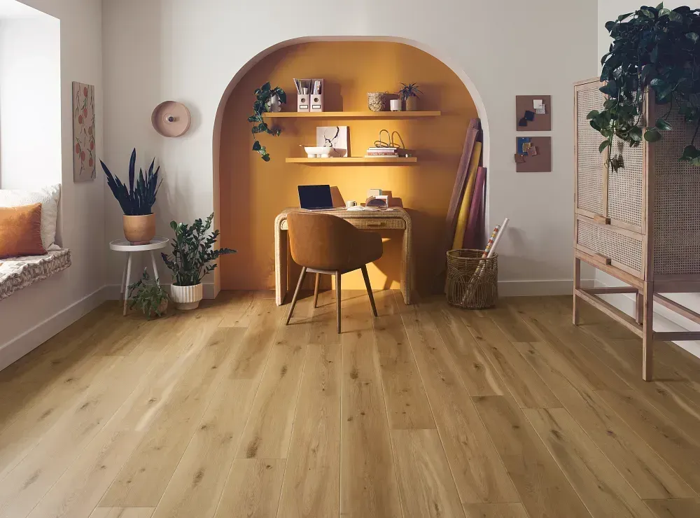 Bright home office with wood floors, desk in a yellow alcove, plants, and a woven cabinet.