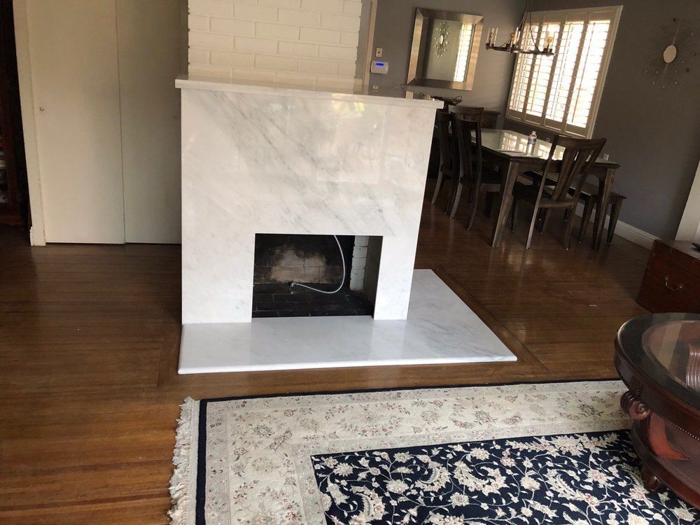 Marble fireplace in a living room with wooden floors, rug, and dining area in the background.