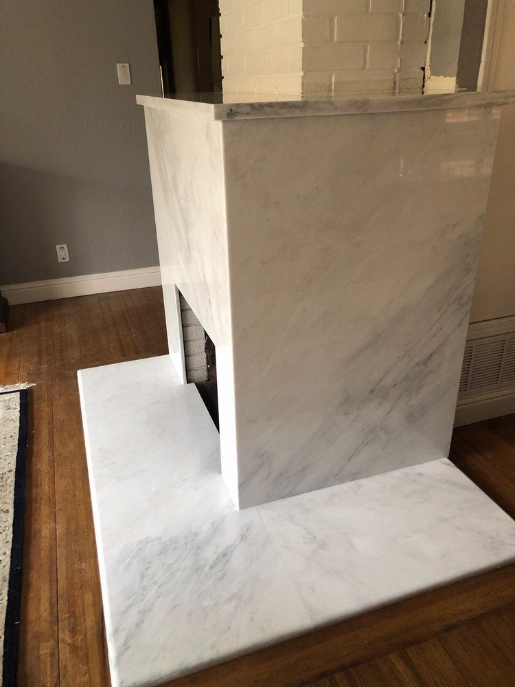 Marble fireplace with gray veining, set against wooden floor and gray wall.