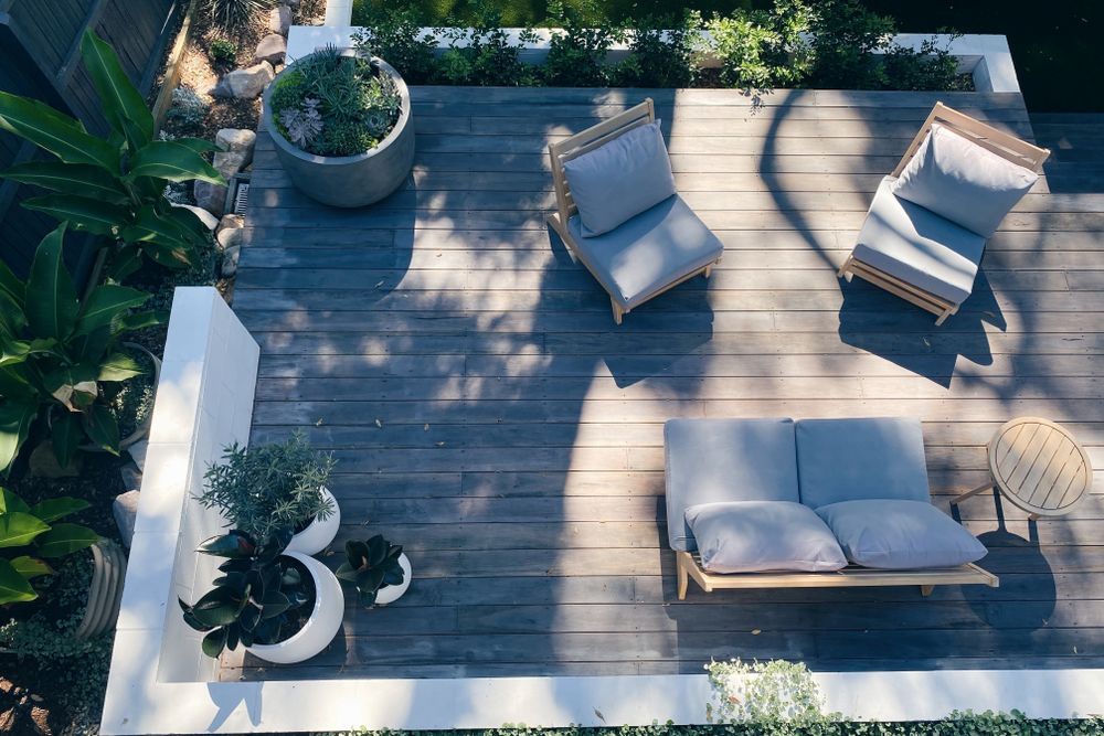 Overhead view of a wooden deck with gray outdoor furniture, potted plants, and a small side table.