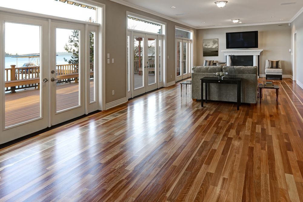 Spacious living room with glossy wood floors, large windows, and a view of a deck and water.
