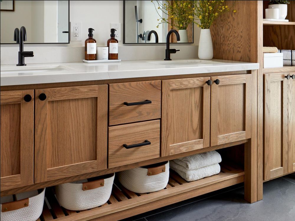 Wooden bathroom vanity with double sinks, black fixtures, and open shelving with baskets and towels.
