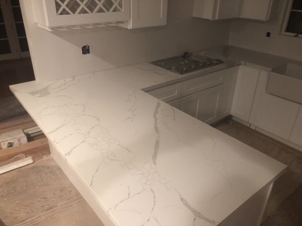 White kitchen countertop with veining, installed on cabinets, next to a stove and a sink.
