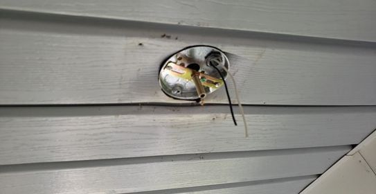 Exposed electrical wiring and fixture on a gray exterior wall.