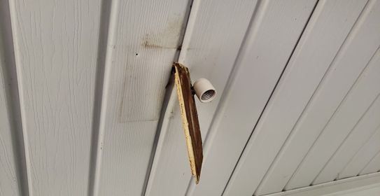 Damaged white ceiling with exposed wood and a security camera.