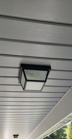 Black square outdoor light fixture on a gray ceiling with horizontal siding.