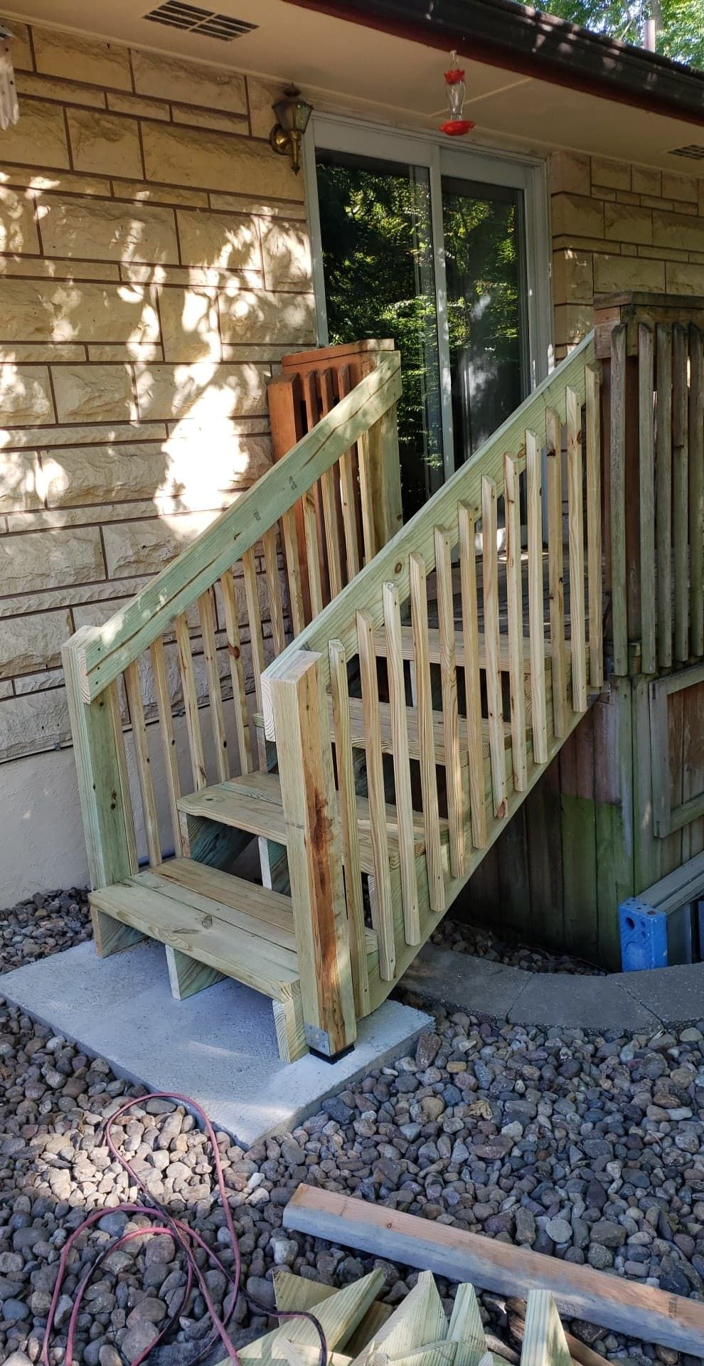 Wooden outdoor steps leading to a sliding glass door, next to a brick building.