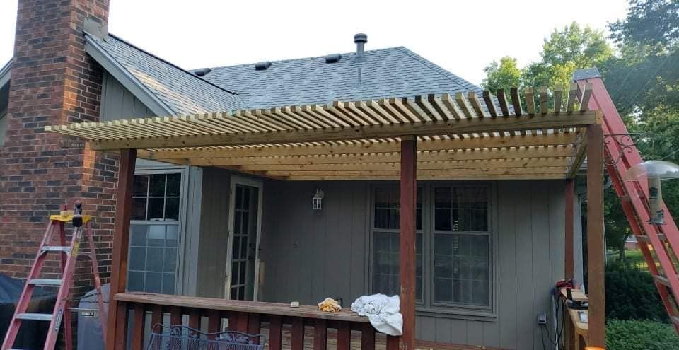 Wooden pergola over a deck attached to a house with a brick chimney.