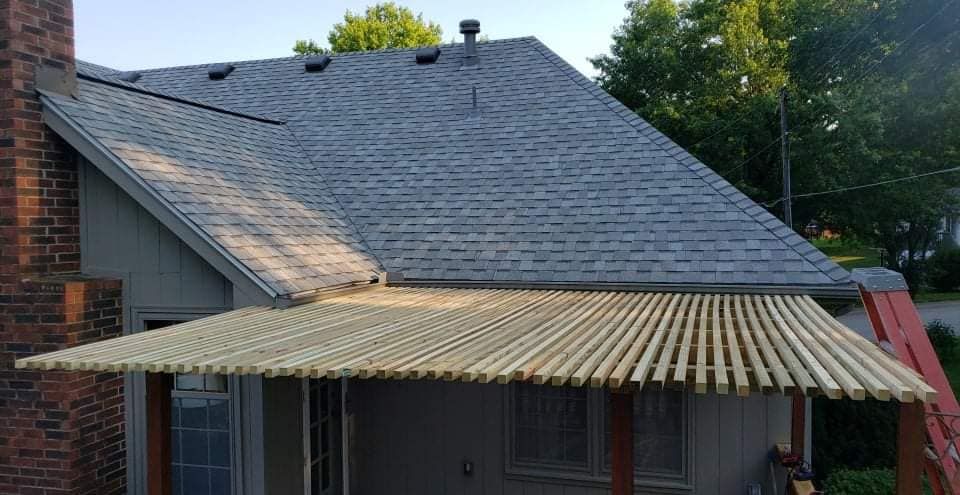 Pergola attached to a house with a gray roof, brick chimney, and a ladder.