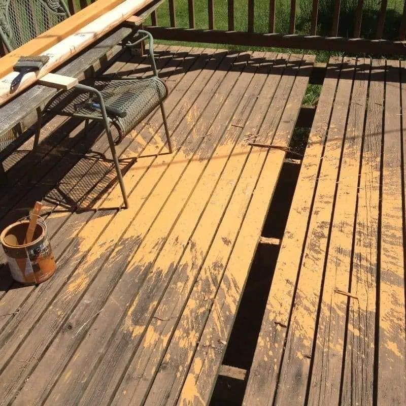 Deck with peeling yellow paint, a metal chair, and paint can in sunlight.