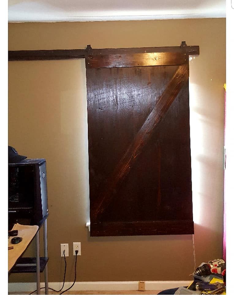 Barn door, brown, mounted on wall, with sliding hardware. Beige wall. Dark wood door.
