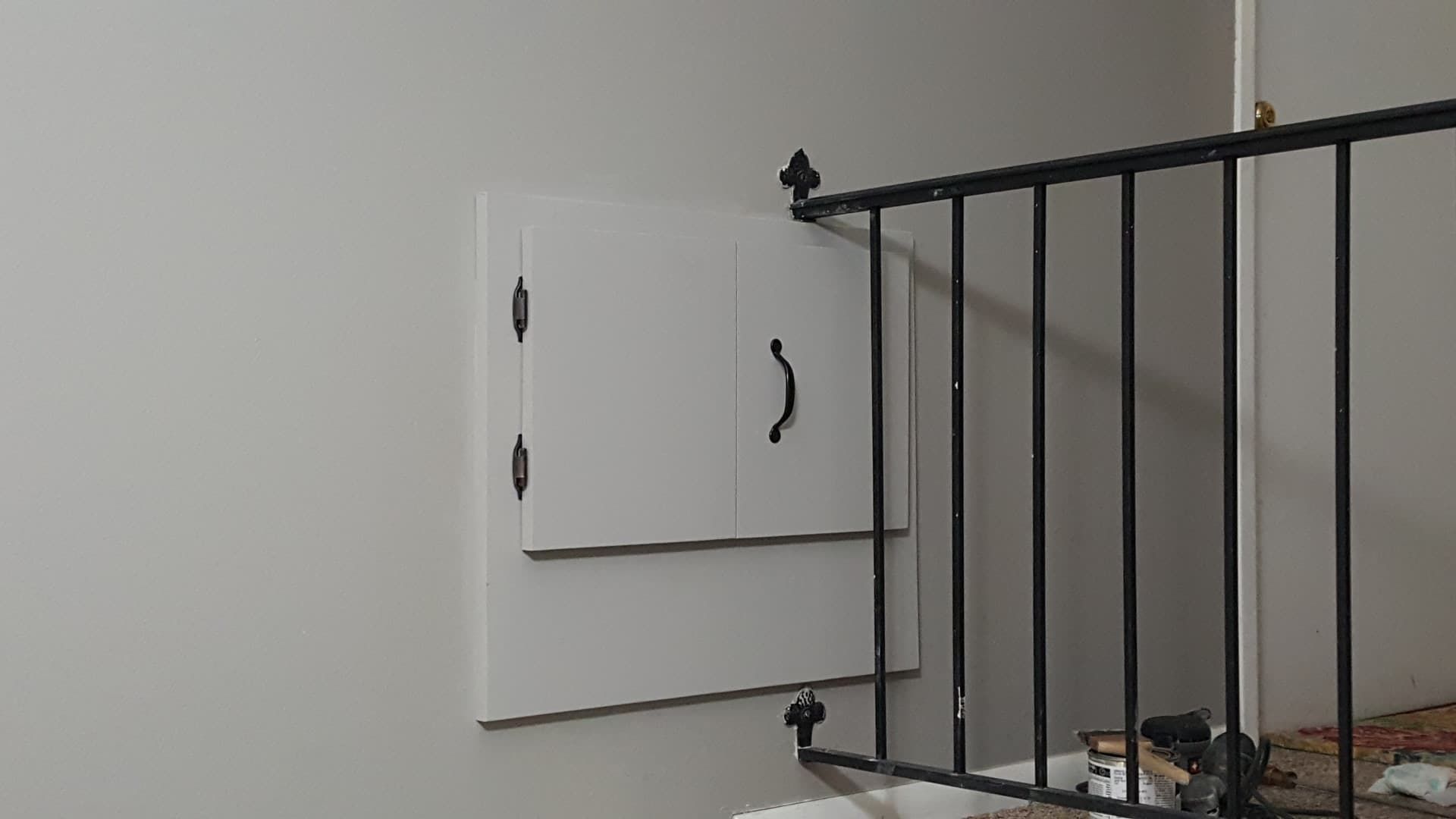 White cabinet on a gray wall next to a black railing, potentially on a landing.