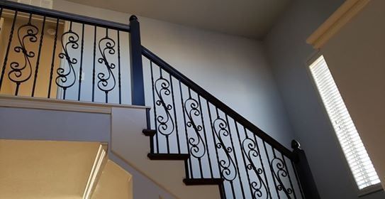 Staircase with black iron railing and dark wood steps against a light gray wall.