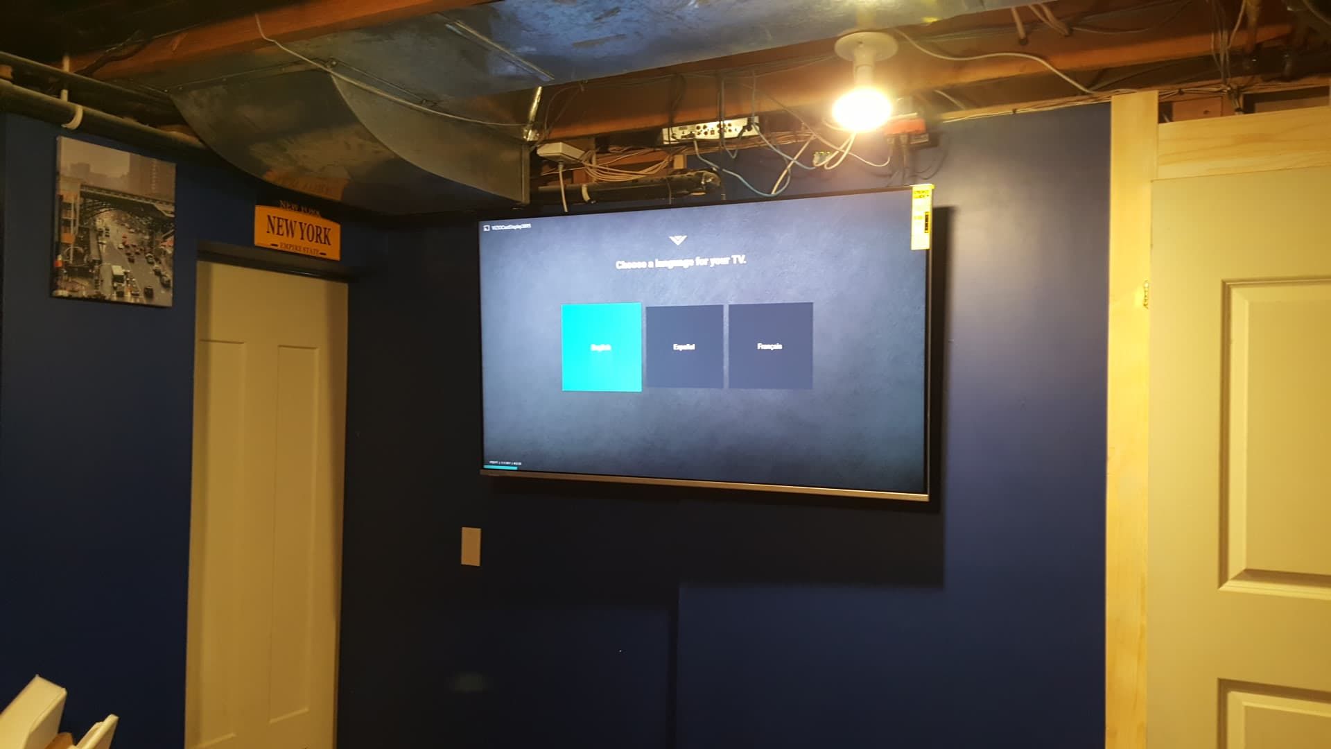 TV mounted on a dark blue wall in a basement, with a lightbulb overhead and a white door to the right.