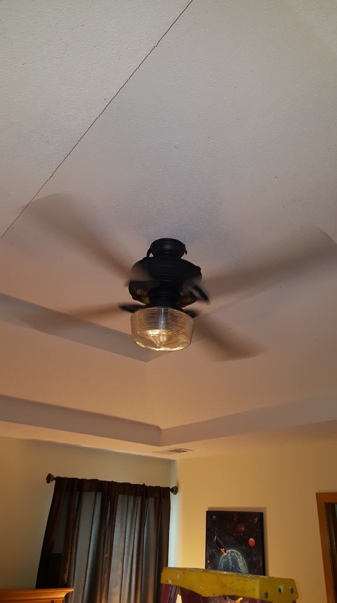 Ceiling fan with light fixture, mounted on a white ceiling with dark beams, near a window and painting.