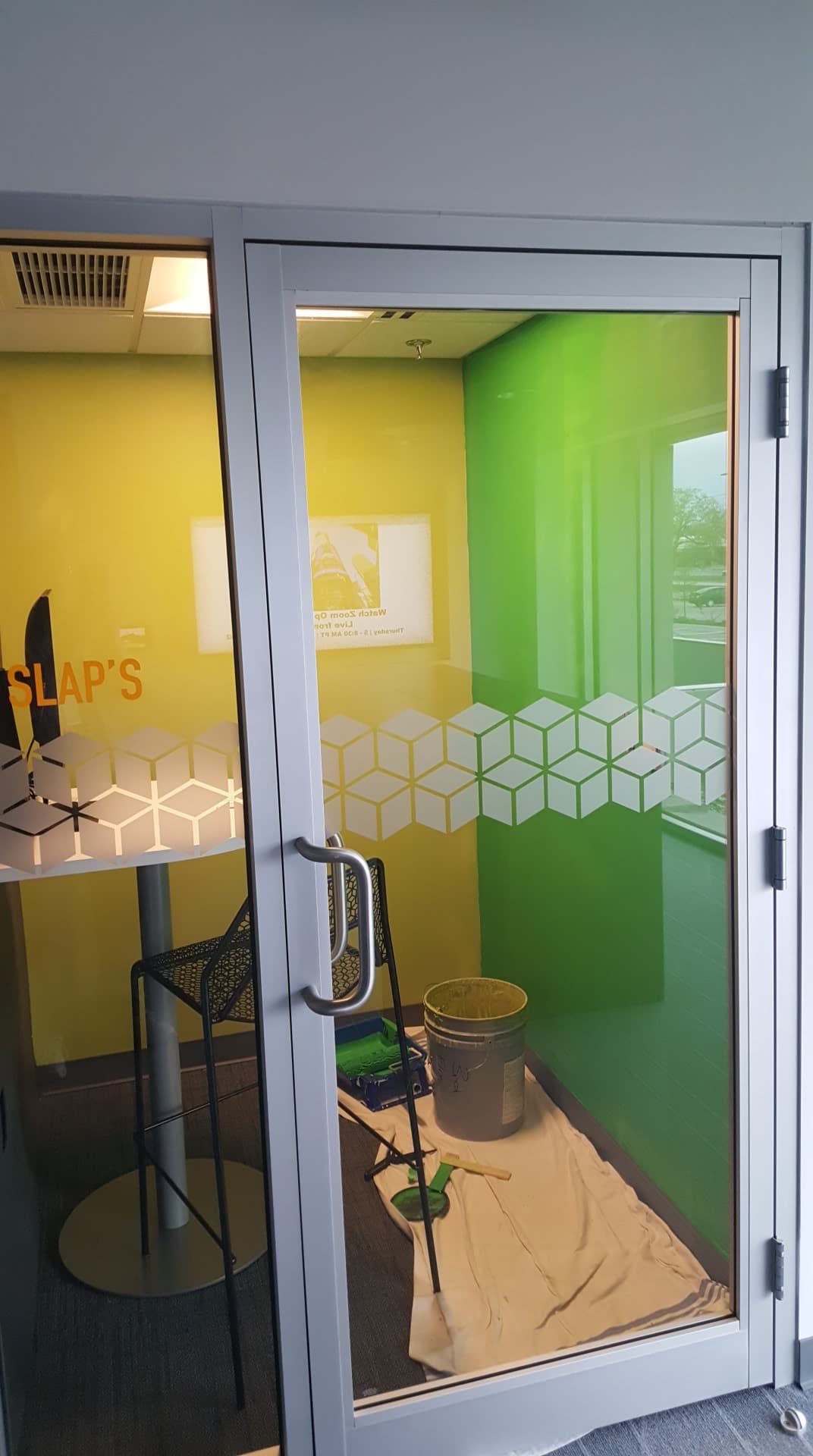 Glass door leading to a small, lime green and yellow room. Inside, a stool with a plant.
