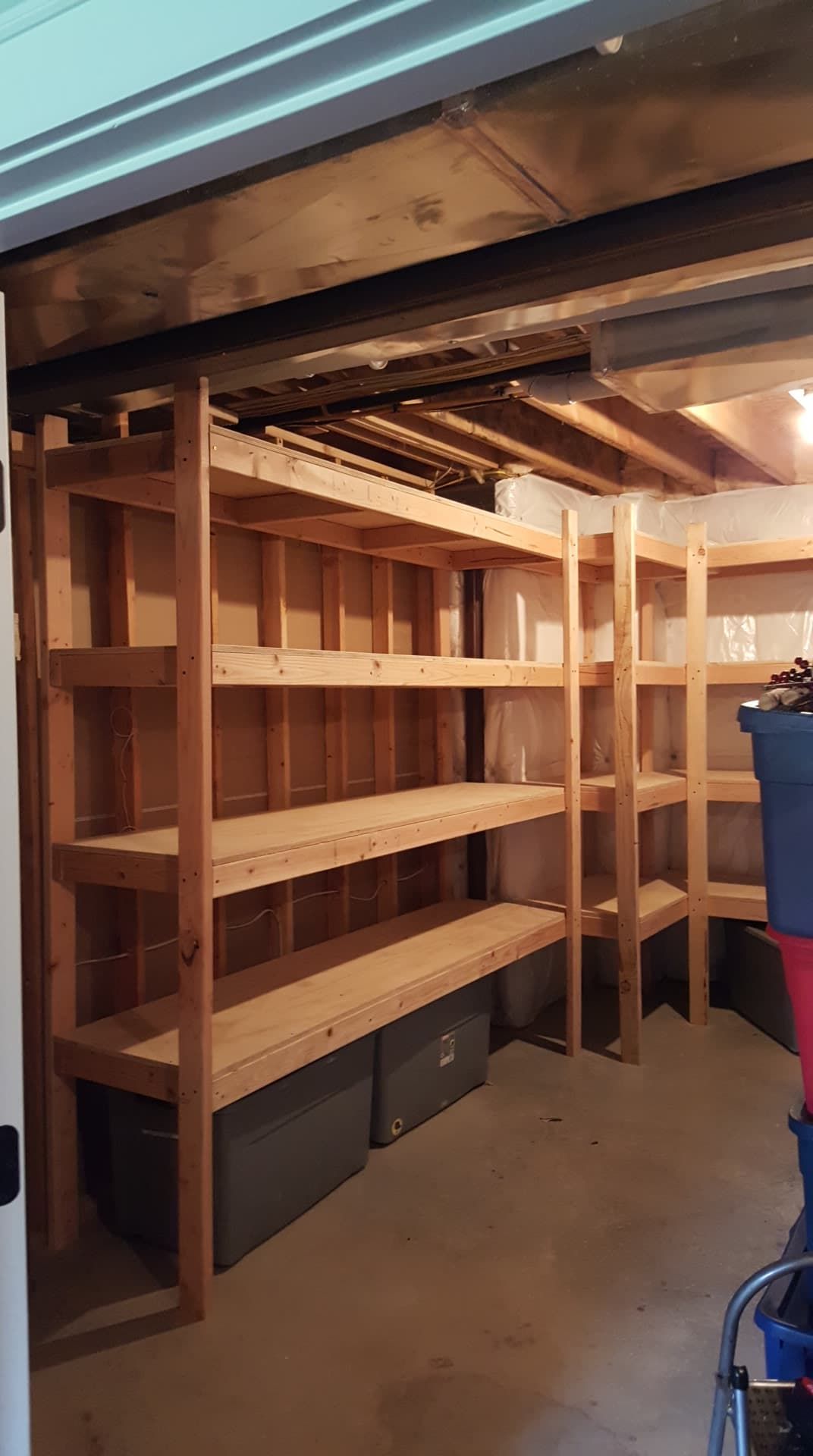 Wooden shelves in a basement, holding storage bins. Brown beams and a concrete floor.